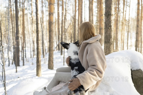 Unrecognizable woman holding a border collie in a snowy forest, sharing a peaceful moment