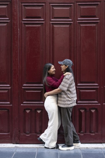 A loving moment between latin lesbian couple, embracing in front of a deep maroon door. The image captures a sense of intimacy and connection, reflecting love and partnership