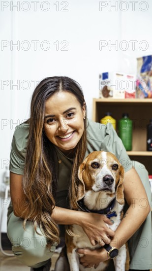 A nutritionist smiles warmly, embracing a beagle in an office setting. Shelves with nutritional products are visible, highlighting a focus on pet wellness and care