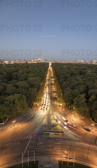 An aerial view of Berlin's Strabe des 17 Juni at dusk, featuring a tree-lined boulevard illuminated by streetlights and extending towards the Berlin TV Tower under a clear evening sky