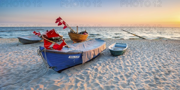 Fishing boats with red flags on fine sandy beach at sunrise, Baltic resort Kölpinsee, Usedom island, Mecklenburg-Western Pomerania, Germany