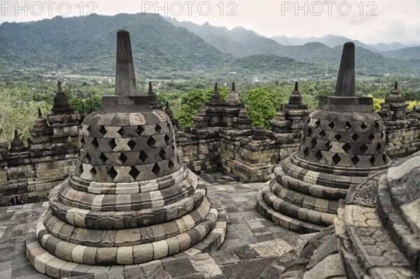 Majestic view of the Borobudur Temple's ancient stone stupas, with vibrant green mountains and lush scenery in the background, highlighting Indonesia's cultural heritage