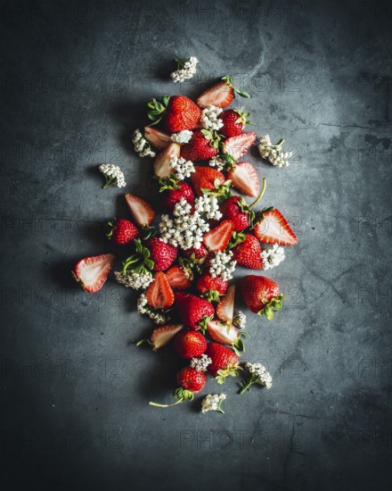 A visually striking arrangement of ripe strawberries beautifully scattered on a dark stone surface, enhanced by delicate white flower accents for a natural touch