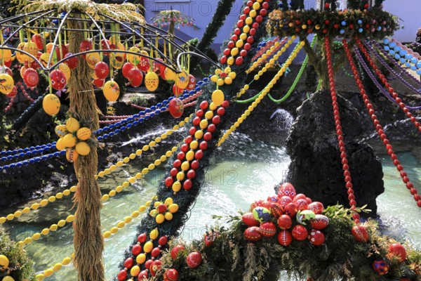 Easter fountain, Franconian Switzerland, Bieberbach, Egloffstein market, Forchheim district, Upper Franconia, Bavaria, Germany, garlands of colorful eggs are stretched over a fountain, a fountain is festively decorated with colorful eggs and cheerful colors, over water