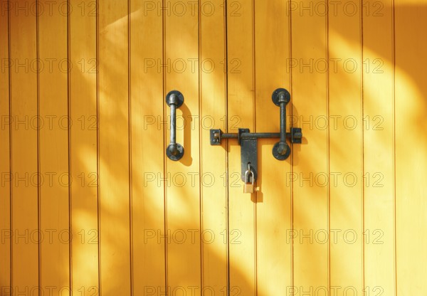 Yellow wooden door in California, USA, featuring strong metal handles and a padlock. Sunlight casts soft patterns, creating a vibrant and secure atmosphere