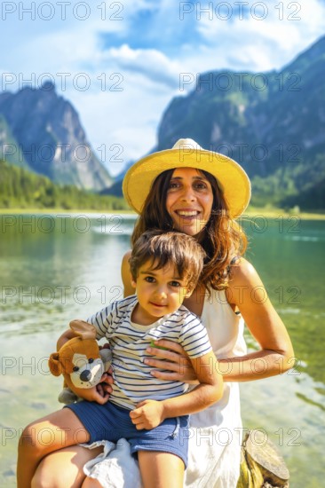 Mother holding her son while enjoying a sunny summer day at lake dobbiaco with the dolomites in the background