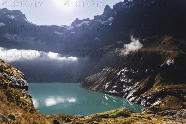 A stunning turquoise crater lake at El Altar volcano, Ecuador, surrounded by rugged peaks, golden sunlight, and misty clouds, creating a dramatic and serene Andean landscape