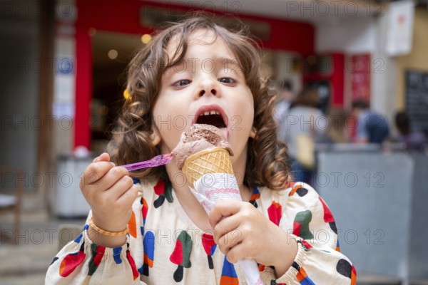 A young girl delights in a chocolate ice cream cone, savoring every bite on a sunny day in a picturesque village, capturing a moment of pure joy and innocence
