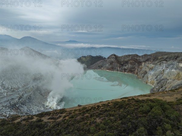 Drone view of Ijen crater in Indonesia with turquoise acidic lake and visible sulfur smoke near the shore