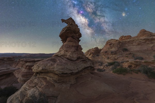 A breathtaking view of a starlit sky over unique rock formations in a desert landscape in Coyote Buttes, Arizona. The Milky Way vibrant colors contrast with rugged terrain, creating a serene scene