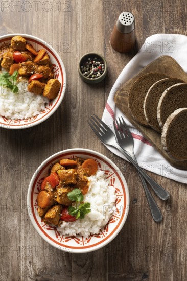 Top view of a bowl of Hungarian pork goulash served with white rice, garnished with a sprig of parsley beside rye bread on a rustic wooden table, with pepper shaker and spices visible. Ideal for a hearty meal