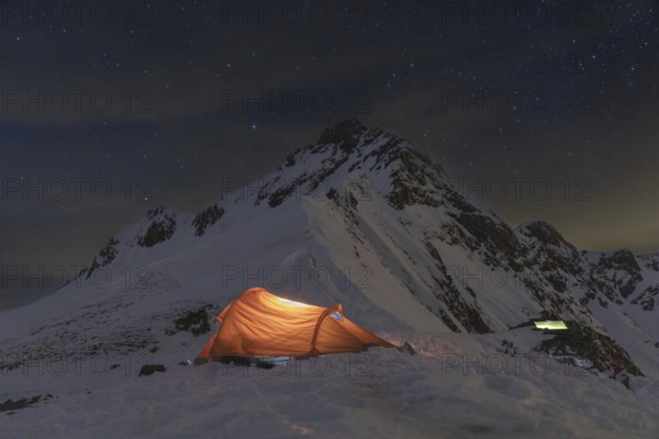A glowing tent in a snowy mountain landscape under a starlit sky. Perfect for ski touring and winter adventures, this serene setting captures nighttime wilderness beauty