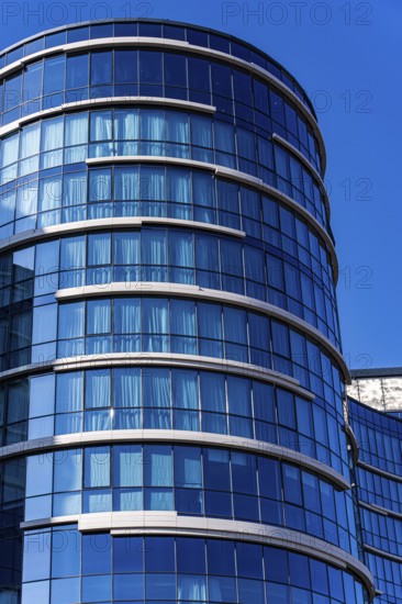 A stunning example of modern architecture featuring a curved glass facade with visible concrete and metal elements, set against a vivid blue sky