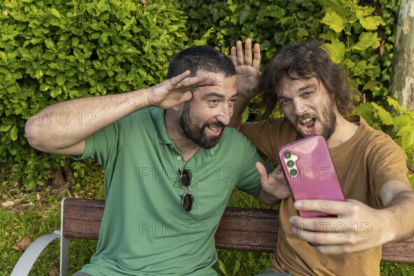 Two friends have fun taking a playful selfie while sitting on a park bench The man in green, who is blind, smiles and poses enthusiastically alongside his friend, celebrating their joyful bond