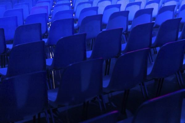 A series of empty blue chairs are arranged in neat rows under a dramatic blue spotlight at a conference of AI in Amsterdam, creating a cool and contemporary atmosphere
