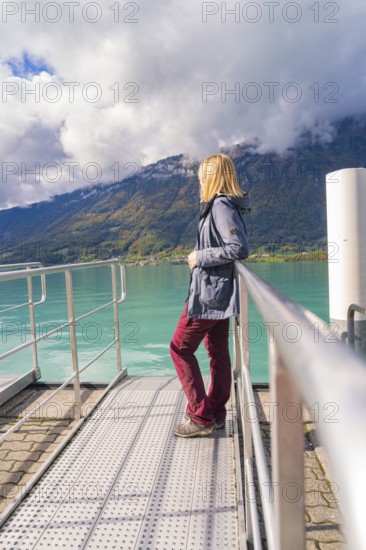 Woman in casual clothes leaning on the railing of a jetty with a view of the lake and mountains, Lake Brienz, Switzerland