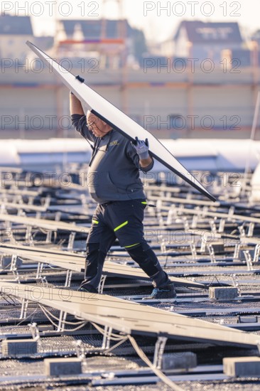 Worker lifts a large solar module on a roof, PV assembly at OBI Baumarkt, Mühlacker, Enzkreis, Germany