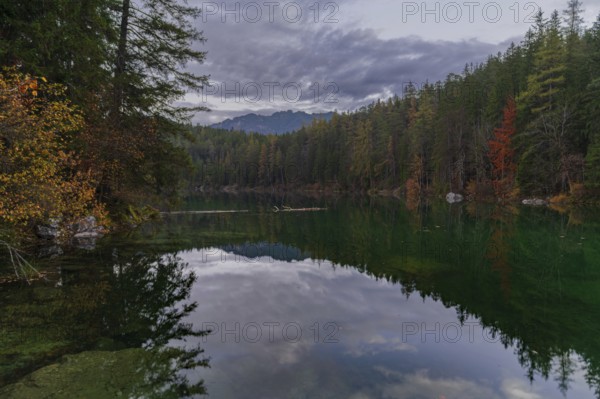 A tranquil lake in the Bavarian Alps, Eibsee, reflects the vibrant colors of autumn Dense forest borders the lake, creating a peaceful and picturesque scene