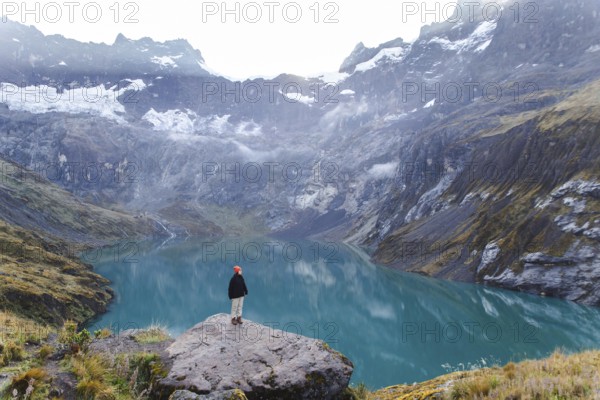 A woman stands on a rocky ledge, overlooking the stunning turquoise lake and surrounding peaks of El Altar volcano in Ecuador, embodying the spirit of adventure