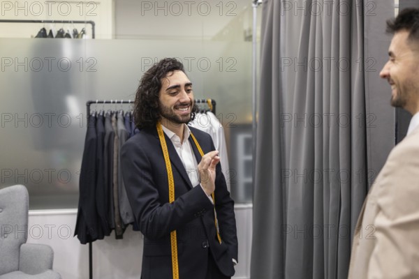 A tailor communicates with a customer in a suit store, showcasing a friendly ambiance. Suits hang in the background, highlighting the tailor expertise and the shop selection