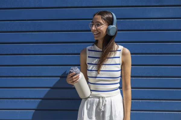 Smiling woman enjoying her active outdoor lifestyle in the city, wearing headphones and holding a water bottle. She dressed casually, embracing the urban vibe