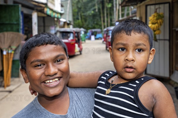 Two young boys pose happily on a street, one smiling, the other seriously, A family in Ratnapura in Sri Lanka