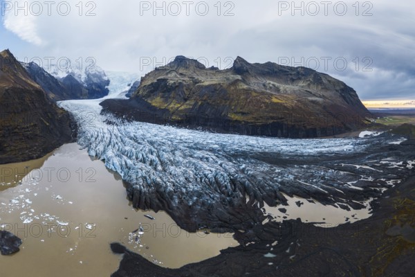 A panoramic shot of the vast Vatnajökull Glacier flowing between rugged mountains under a cloudy sky in Vatnajökull National Park, Iceland