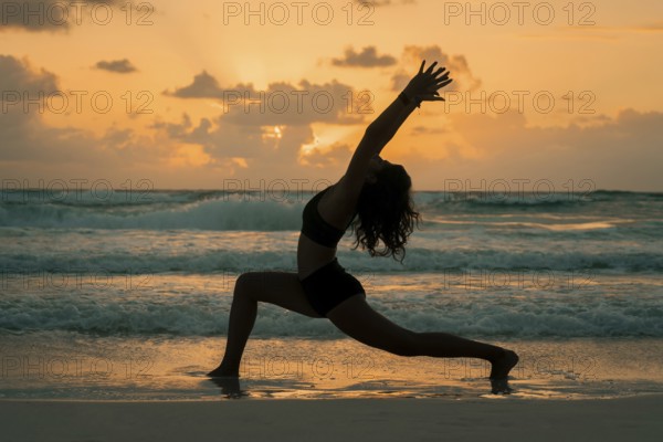 A woman practices yoga on a beach at sunrise, striking a graceful pose that symbolizes balance, serenity, and a deep connection with nature amidst the waves and morning light in Tulum, Mexico
