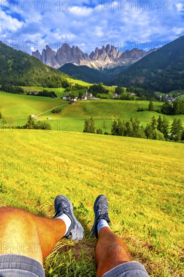 Tourist resting on a green meadow, enjoying the breathtaking view of the idyllic valley and the iconic st. Magdalena church in the italian dolomites