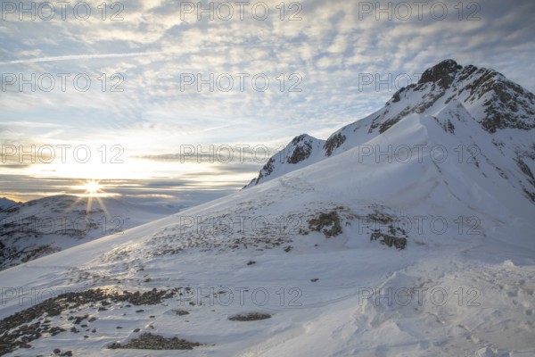 Scenic winter landscape with snow-covered mountains perfect for ski touring. The sunrise casts a warm glow over the peaks, creating a serene and majestic atmosphere