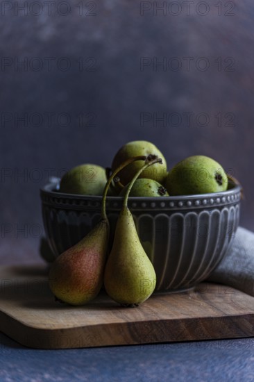 A collection of fresh wild pears displayed in a decorative ceramic bowl, resting on a wooden board. The rustic setting highlights the natural beauty of the fruit