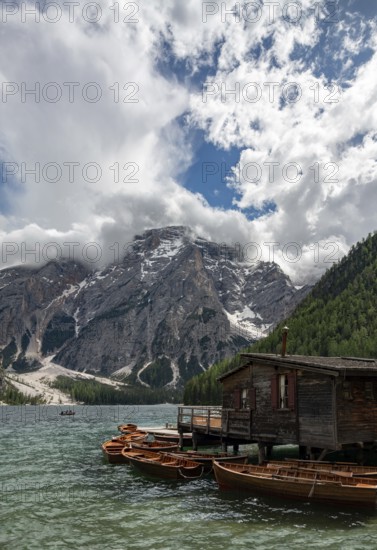 Traditional wooden rowboats rest near a rustic wooden boathouse on Lago di Braies, surrounded by dramatic cliffs and snow-capped peaks in the Dolomites, Italy