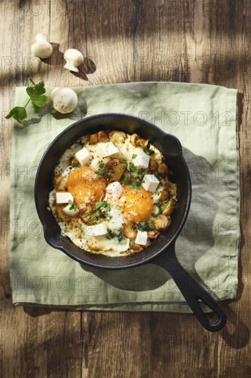 Fried eggs with spinach, mushrooms, grated cheese and feta cheese in small cast iron skillet. Top view