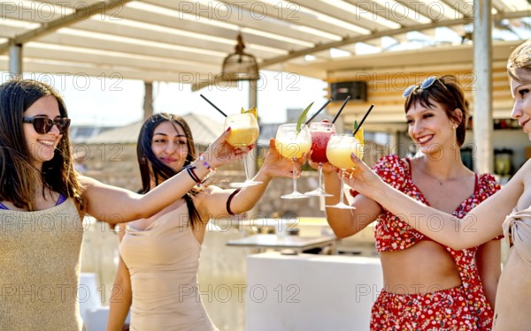 Four friends gather at a beach bar, raising their cocktails in celebration on a sunny summer day. The vibrant drinks add to the joyful atmosphere by the sea