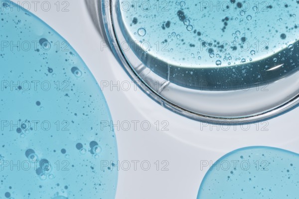 A close-up image of vibrant blue cosmetic gel droplets with visible texture and bubbles, set against a clean white background, capturing the beauty of skincare products