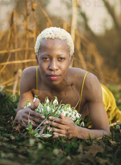 A serene woman lies in the grass, surrounded by delicate snowdrops in Tacony Creek Park. Her peaceful expression complements the tranquility of the natural setting, emphasizing harmony with nature