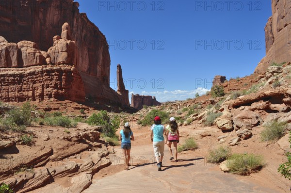 Three people hiking in a vast desert landscape with impressive red rock formations, Arches National Park, Utah, USA