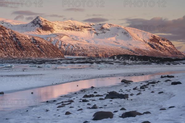 Majestic Icelandic landscape with sunset hues on snow-covered peaks, reflected in icy waters. A stunning display of nature in Iceland's winter wonderland setting in Skaftafell