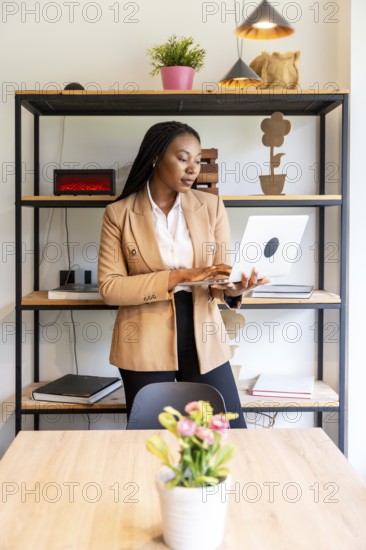 Businesswoman standing in an elegant hotel room, using a laptop to manage her business efficiently while traveling for work