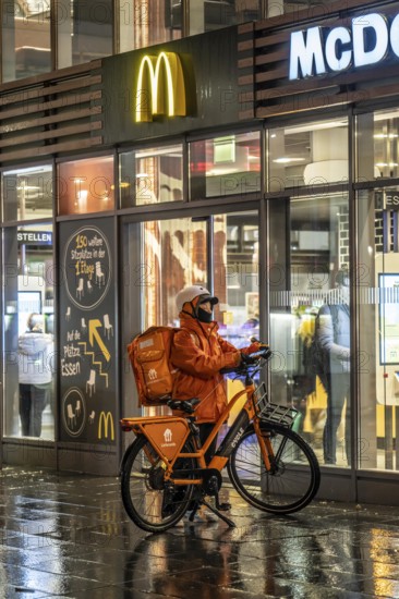 Street at the main station, Lieferando courier, cyclist, rainy weather, city centre, in the evening, Essen, North Rhine-Westphalia, Germany