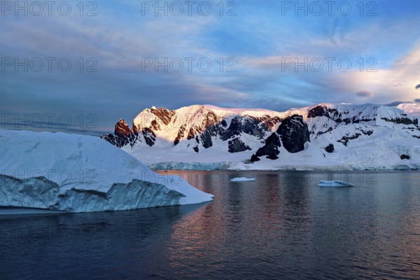 Iceberg and mountains reflected in the water at dusk, icebergs in the Southern Ocean in Antarctica