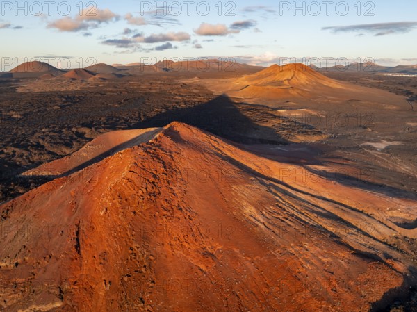 Picturesque volcanic landscape in evening light, red volcano Montaña Bermeja between lava fields, aerial view, Lanzarote, Canary Islands, Spain