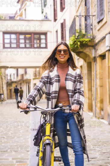 Pretty latin woman with sunglasses doing bicycle sightseeing in the city through the old town. Eco tourism in spring on vacation, model smiling