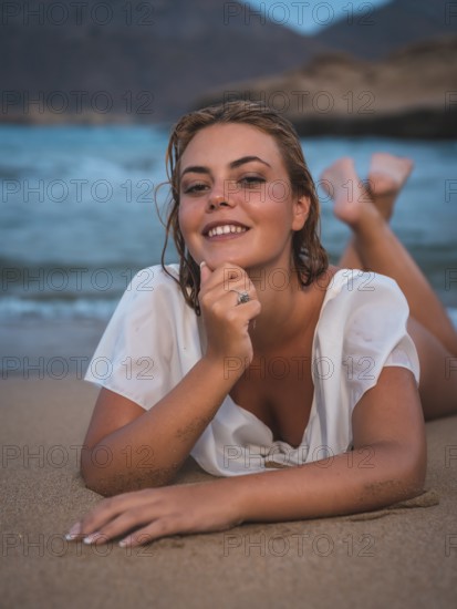 Lifestyle of a blonde Caucasian girl in a white swimsuit. Smiling in the sand after getting out of the water with the sea in the background
