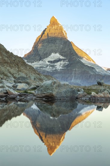 Majestic view of the Matterhorn in the Swiss Alps reflecting in calm waters. The iconic pyramid shaped peak stands tall against a clear blue sky, showcasing natural beauty