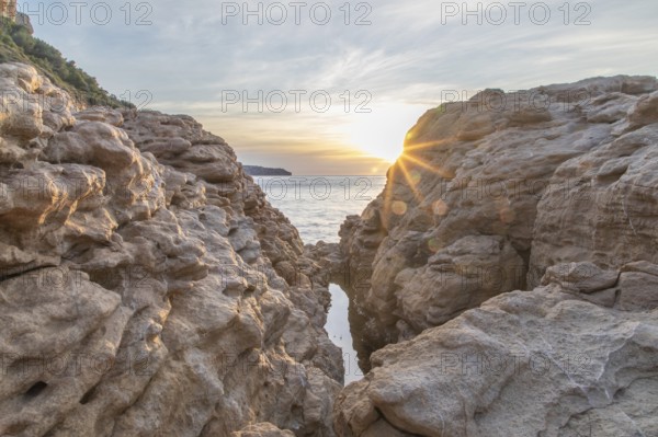 Stunning view of the sun setting over the Mediterranean Sea, seen between rocky formations on the Costa Blanca. The golden light creates a serene and tranquil landscape