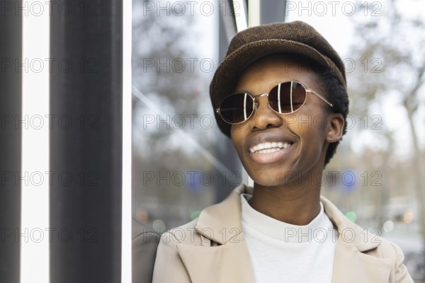 A fashionable black woman wearing sunglasses and a hat, smiling confidently in an urban setting Her stylish outfit and accessories highlight her vibrant personality