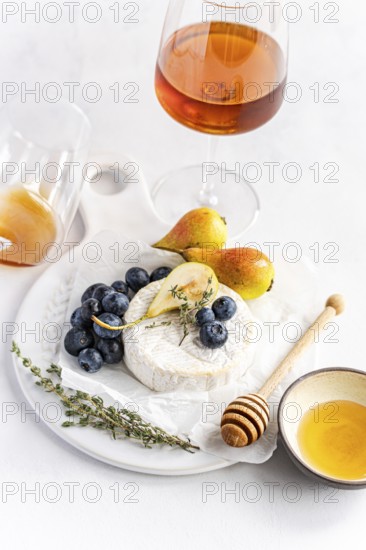 Elegant cheese platter with creamy brie, ripe pears, and juicy blueberries, accompanied by a glass of amber wine on a white table, offering a sophisticated culinary presentation