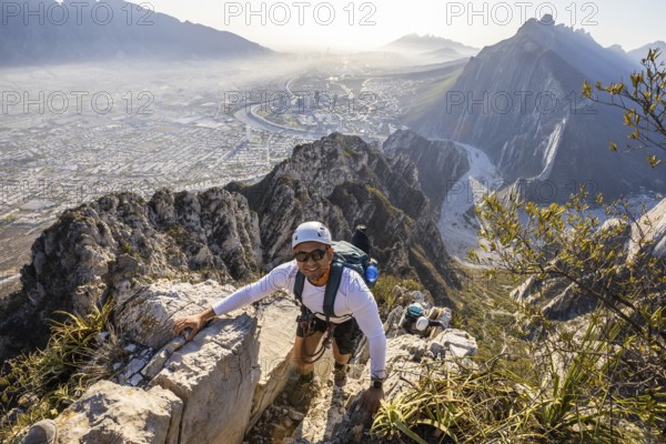 A man skillfully practices mountaineering and rappelling at Eagleâ€™s Nest in Monterrey, Mexico, with a breathtaking cityscape view in the backdrop on a clear day