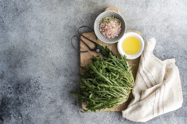 Fresh arugula, Himalayan pink salt, and olive oil arranged on a rustic wooden cutting board with vintage scissors and a linen towel, styled for a natural kitchen aesthetic
